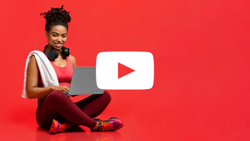 Woman sits in workout clothes with laptop in a totally red abstract space ready to login to YouTube to do her YMCA workouts