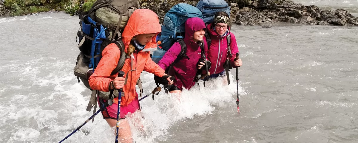 Three backpacking teens crossing a river