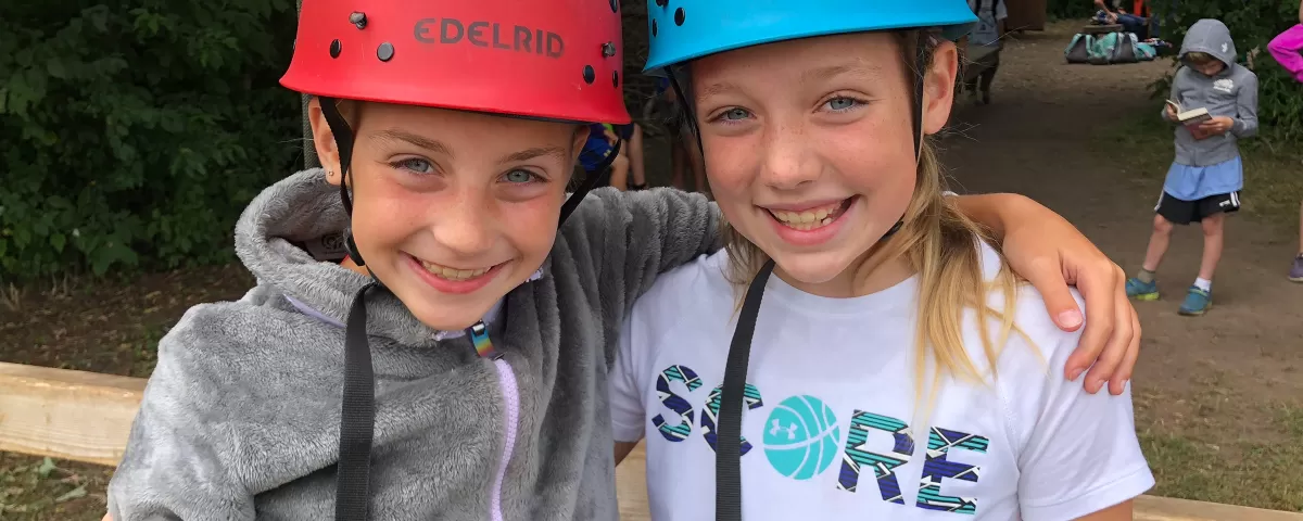 Two girls in climbing helmets smile for the camera