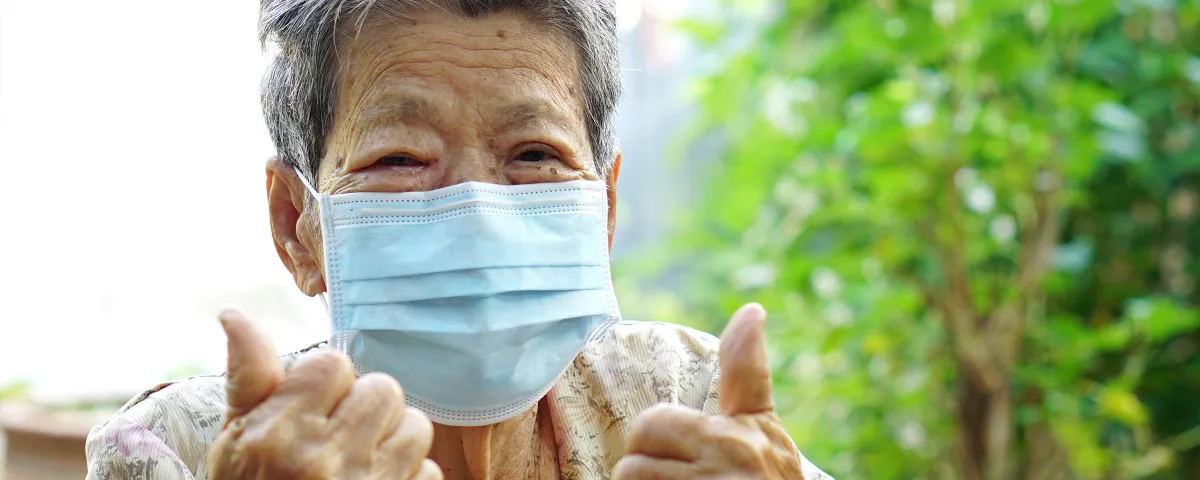 Older woman wearing mask and giving 'thumbs up'