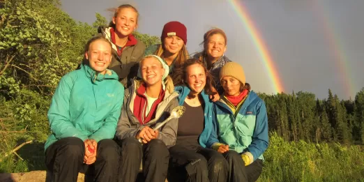 Seven teens sitting under a double rainbow